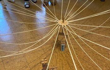 Von oben fotografierte Gruppenübung: Zahlreiche Schnüre verlaufen von einem zentralen Holzstück zu den Füßen der Teilnehmenden. Auf dem Boden liegen mehrere kleine Holzklötze.